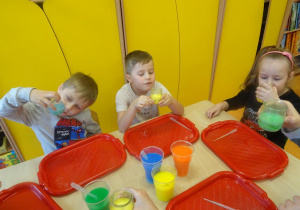 Troje dzieci obserwuje zabarwioną ciesz po wrzuceniu tabletki musującej.